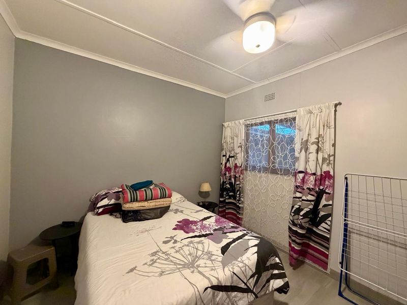 A standard bedroom featuring a ceiling fan, neutral wall finishes, and a window with curtain rod installation.