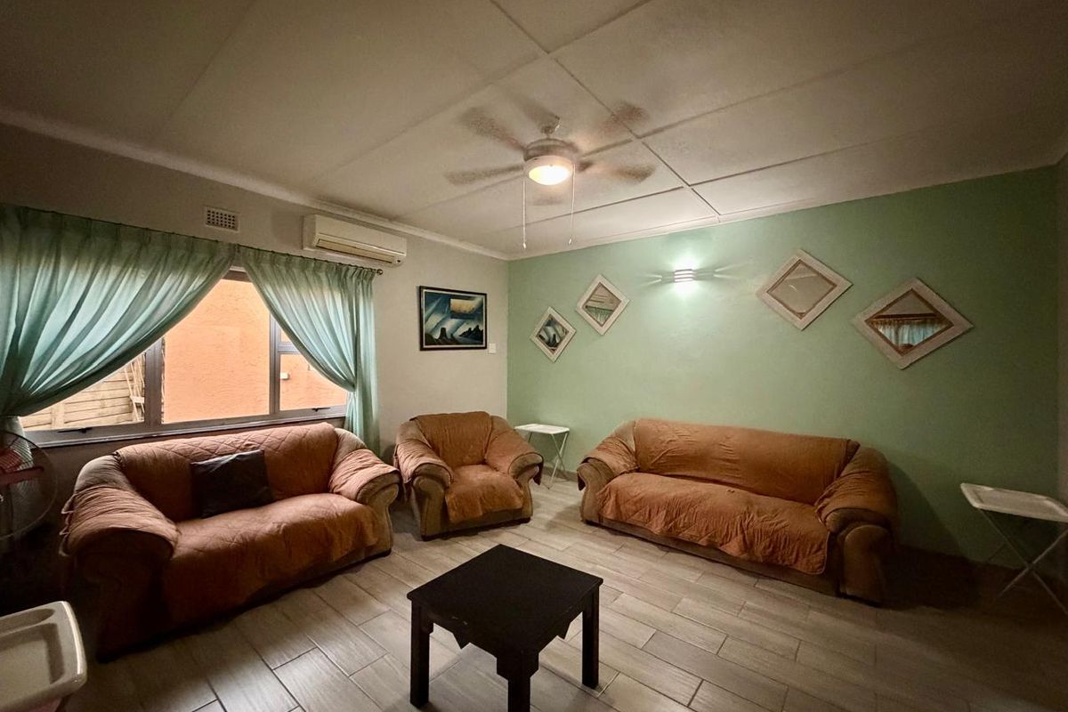A living room featuring tiled flooring, a ceiling fan, and a wall-mounted air conditioning unit.