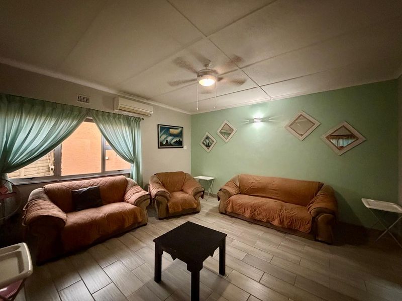 A living room featuring tiled flooring, a ceiling fan, and a wall-mounted air conditioning unit.