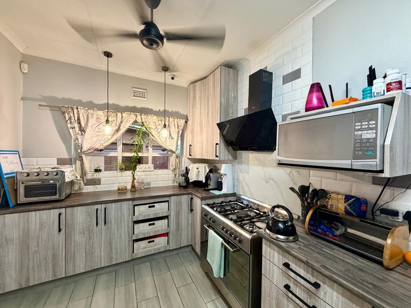 A functional kitchen featuring wood-look cabinetry, subway tile backsplash, gas stove with extractor fan, and built-in microwave, complemented by modern pendant lighting.