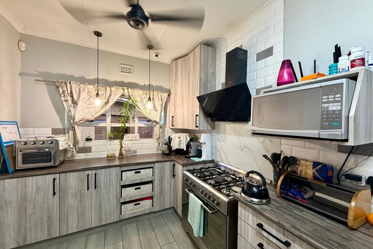 A functional kitchen featuring wood-look cabinetry, subway tile backsplash, gas stove with extractor fan, and built-in microwave, complemented by modern pendant lighting.
