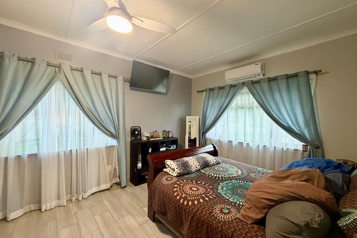 A well-maintained bedroom featuring tiled flooring, a ceiling fan, and a wall-mounted split-system air conditioner.