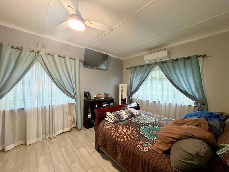 A well-maintained bedroom featuring tiled flooring, a ceiling fan, and a wall-mounted split-system air conditioner.