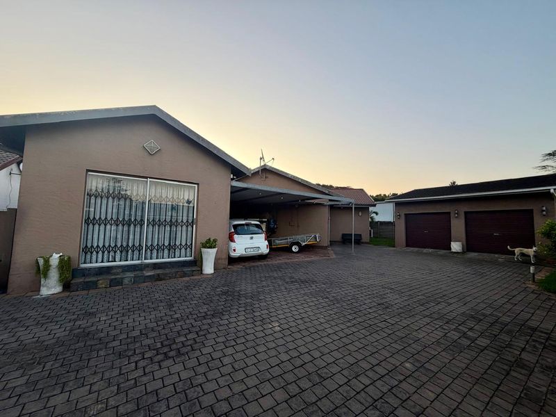 Front view of the property featuring a paved driveway, carport, and a double garage with a well-maintained exterior facade.