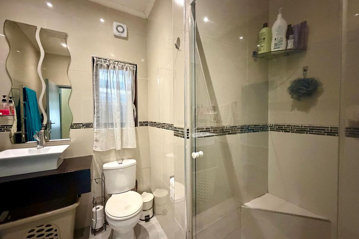 A functional bathroom featuring a glass-enclosed shower with a built-in seat, a vessel sink vanity, and neutral wall tiling.