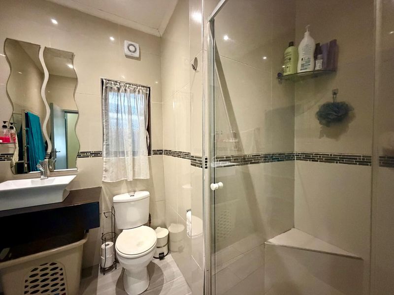 A functional bathroom featuring a glass-enclosed shower with a built-in seat, a vessel sink vanity, and neutral wall tiling.
