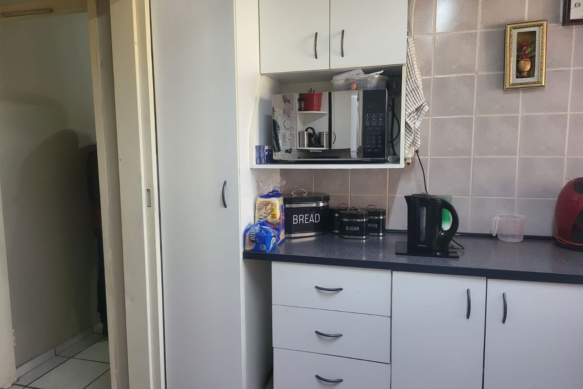 A functional kitchen area featuring white cabinetry, dark laminate countertops, and tiled splashbacks, providing essential storage and workspace.