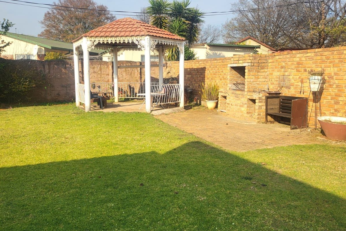 Spacious rear garden featuring a paved patio area, a built-in brick braai, and a covered gazebo structure.