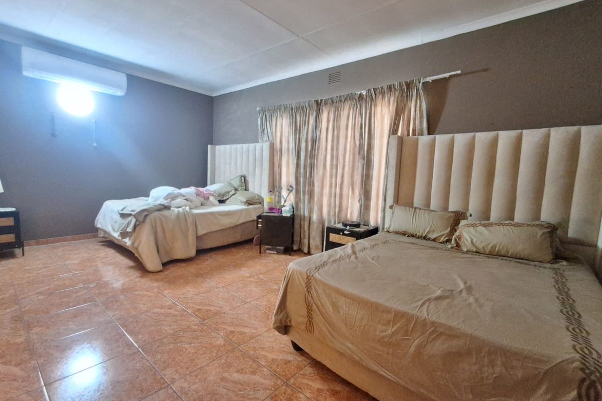 Spacious bedroom featuring tiled flooring, neutral wall tones, and a wall-mounted air conditioning unit.