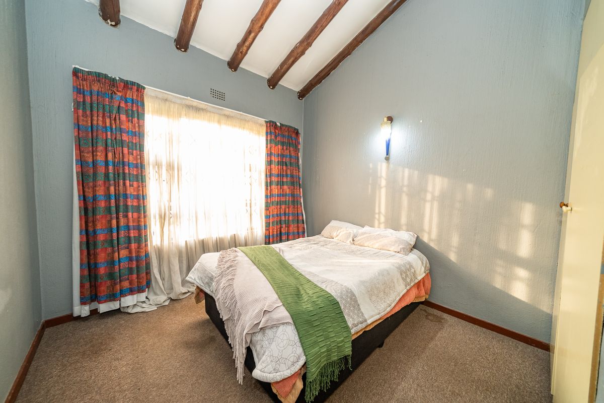 A bedroom featuring exposed timber ceiling beams, textured walls, and carpeted flooring, providing a rustic aesthetic with natural light from the window.