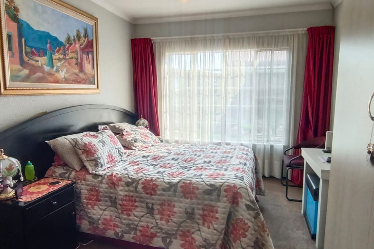 A cozy bedroom featuring built-in cupboards, carpeted flooring, and large windows with curtains, providing ample natural light.