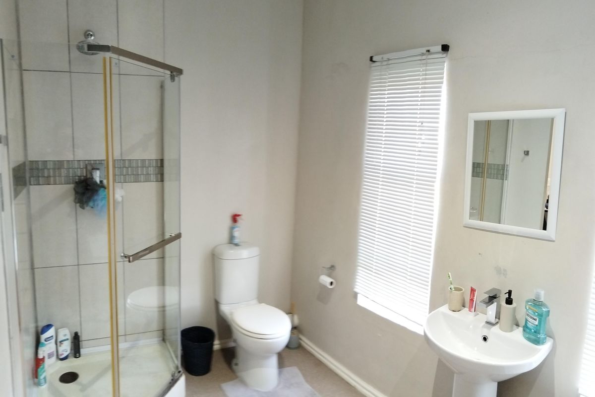 A functional bathroom featuring a glass-enclosed shower, pedestal basin, and toilet, finished with neutral wall tones and tiled shower accents.