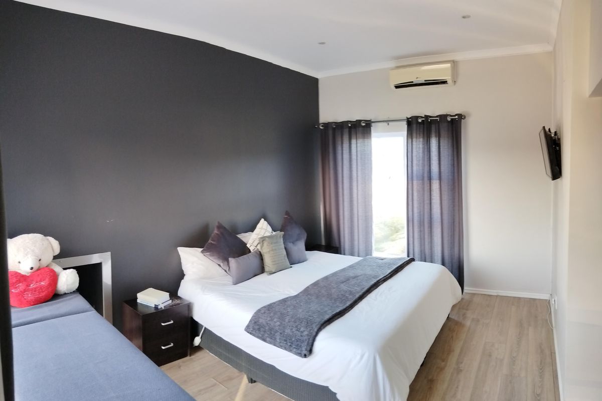 A well-maintained bedroom featuring laminate flooring, an air conditioning unit, and a feature wall, offering a comfortable and functional living space.