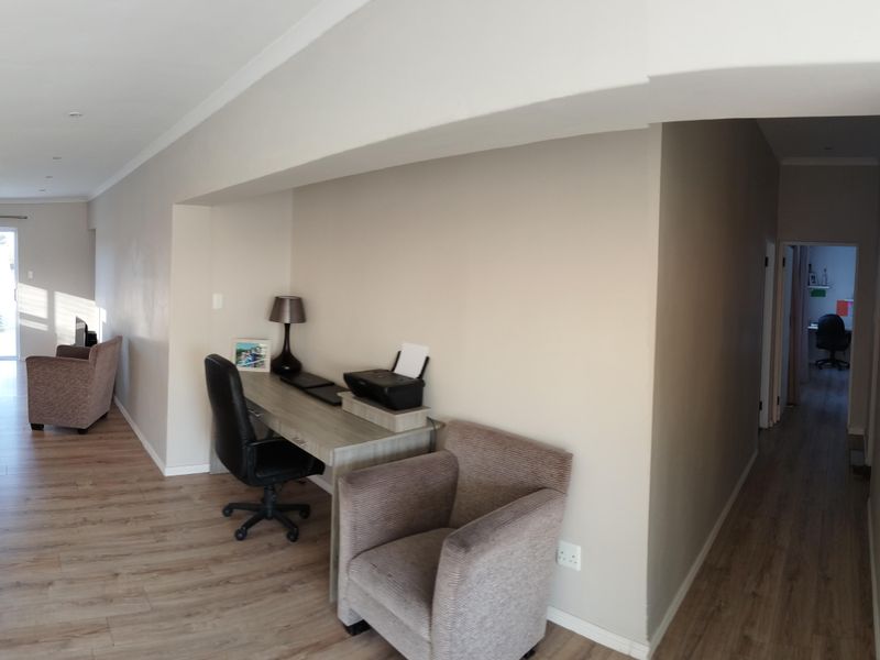 An open-plan living area featuring laminate flooring, recessed lighting, and a neutral color palette, seamlessly connecting to a hallway and adjacent living space.