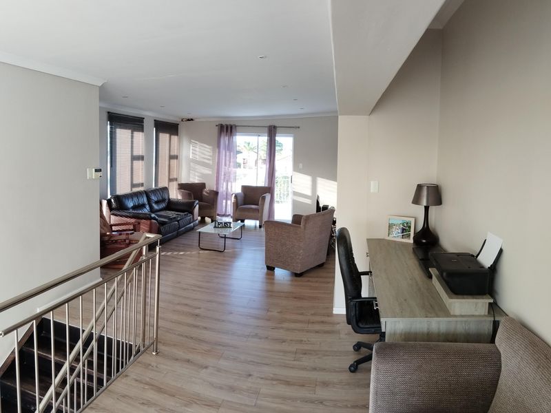 Spacious open-plan living area featuring modern laminate flooring, recessed lighting, and a stainless steel staircase balustrade, leading to a bright outdoor access point.