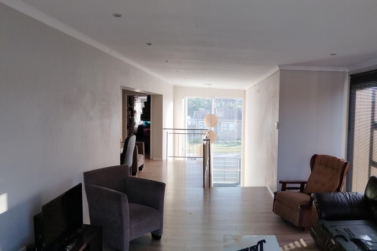 A spacious living area featuring laminate flooring, recessed downlights, and a staircase landing with natural light.