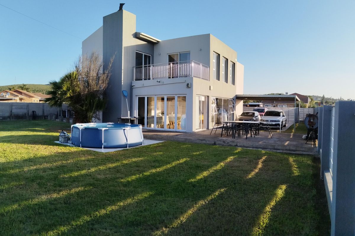 Rear view of a modern two-story house featuring a paved patio, balcony, and a spacious garden area.