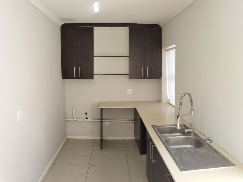 A functional scullery or laundry area featuring dark wood cabinetry, laminate countertops, a double stainless steel sink, and tiled flooring.
