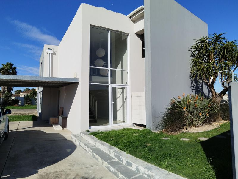 Modern double-story residential facade featuring a prominent glass entrance, concrete driveway, and attached carport.