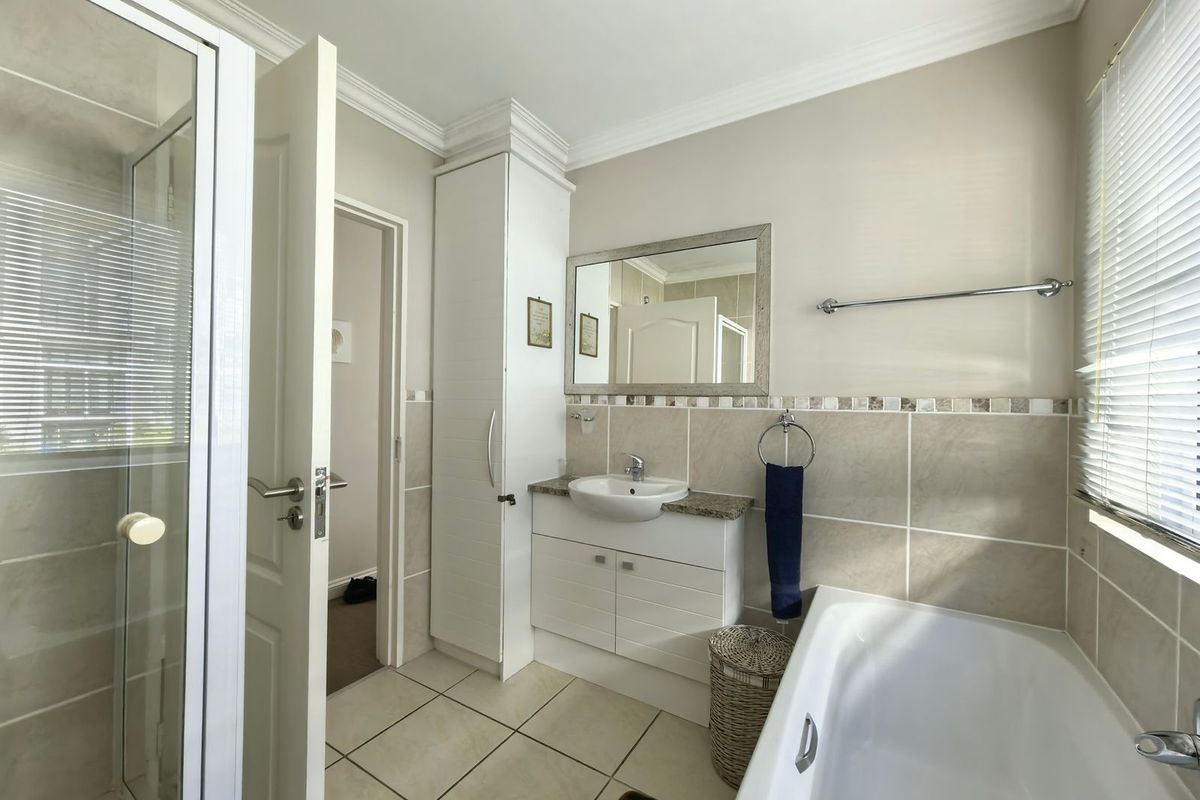 A well-maintained bathroom featuring a built-in vanity with stone countertop, a separate shower enclosure, a bathtub, and neutral wall tiling.