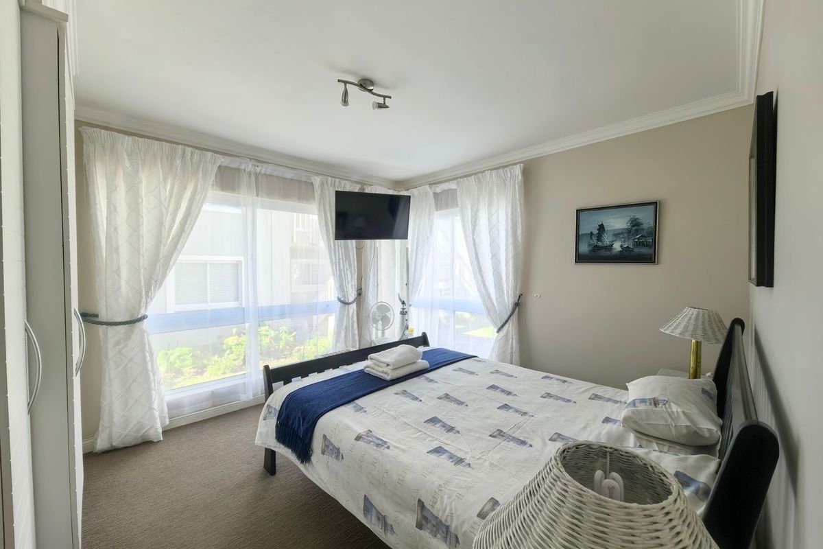 A well-lit bedroom featuring large windows with natural light, neutral wall tones, and built-in wardrobe storage.