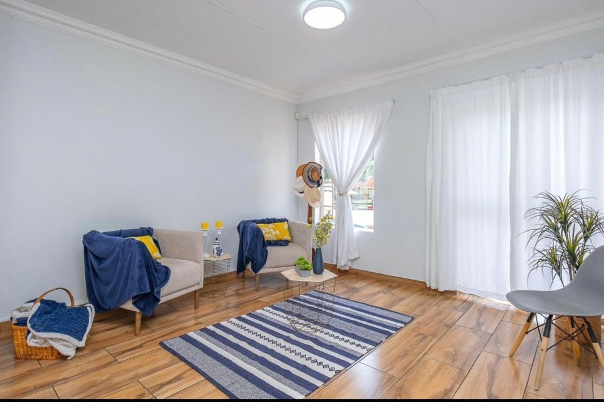 A bright living room featuring wood-look tile flooring, crown molding, and large windows with curtains, providing a comfortable and well-maintained living space.