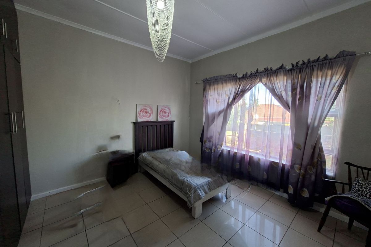 A bedroom featuring tiled flooring, built-in cupboards, and a large window with curtaining, providing natural light.