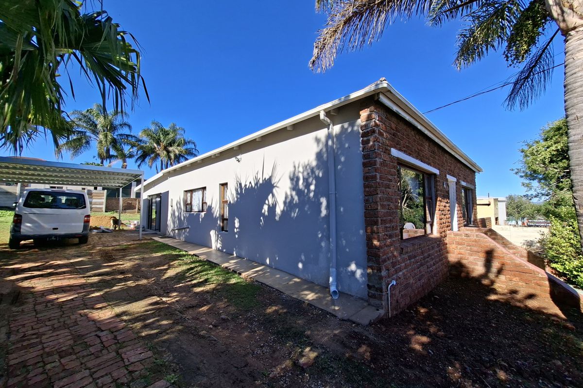 Side view of the house featuring a combination of painted plaster and exposed brick walls, with a paved driveway and metal carport structure.