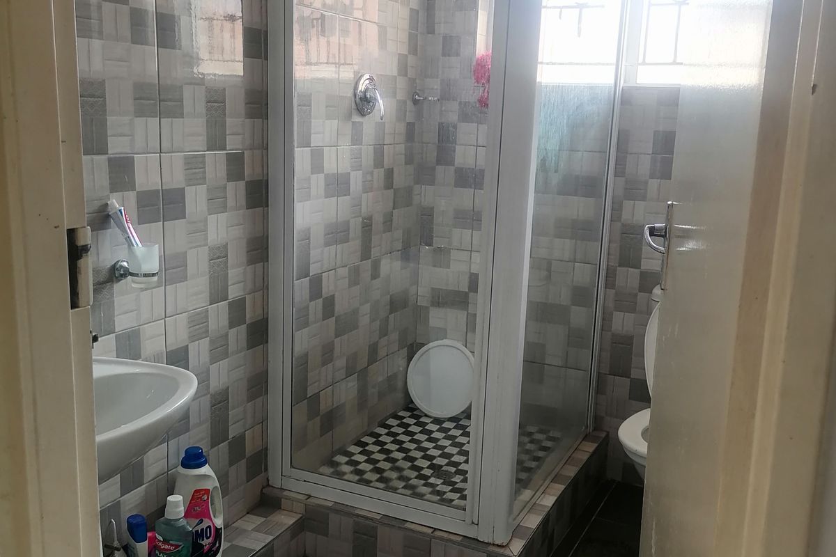 A compact bathroom featuring a raised shower enclosure, pedestal basin, and toilet with full-height wall tiling.