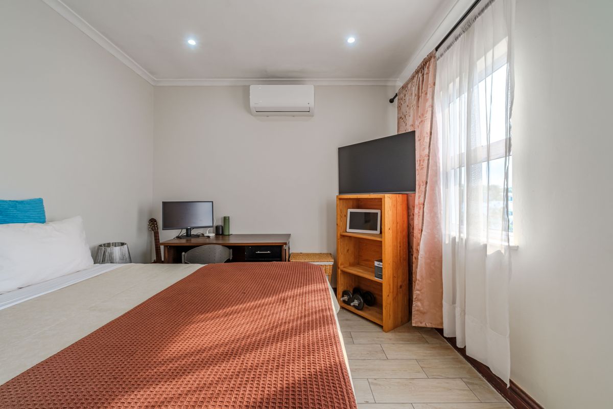 A well-maintained bedroom featuring tiled flooring, recessed ceiling lighting, and a wall-mounted air conditioning unit.