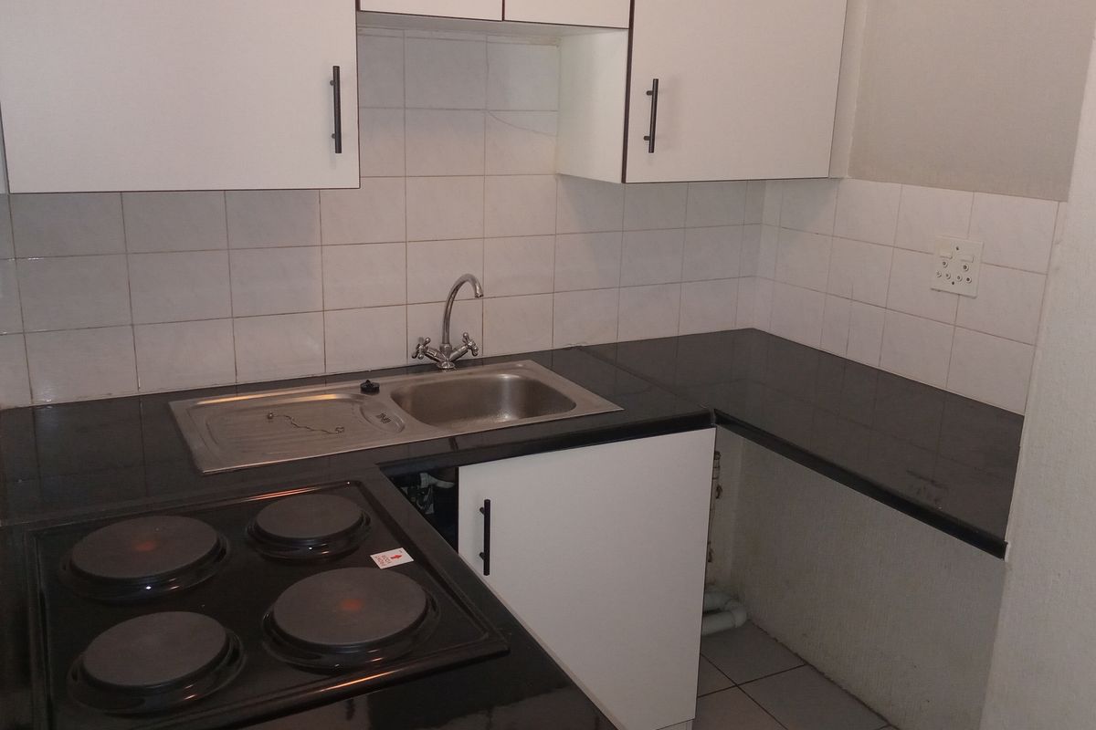 Compact kitchen featuring black countertops, a built-in electric hob, stainless steel sink, and white cabinetry with tiled splashbacks.