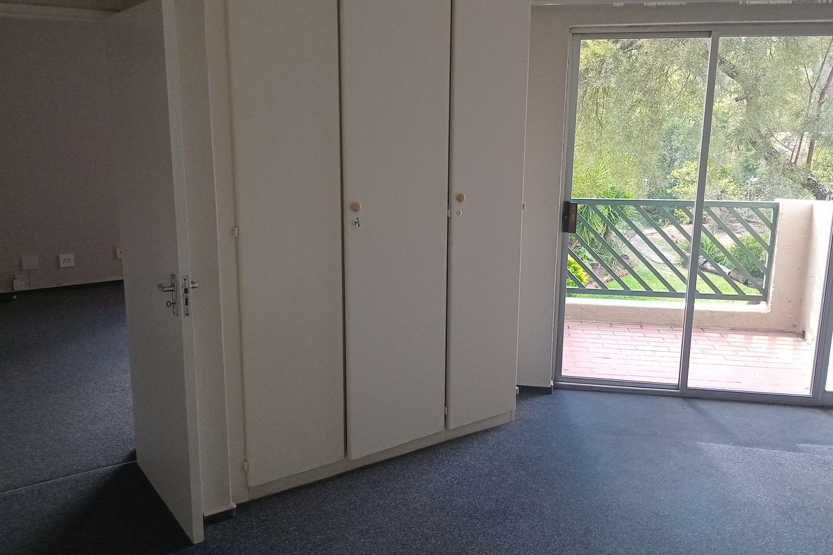 A bedroom featuring built-in cupboards, grey carpeting, and sliding glass doors that open onto a private balcony with garden views.