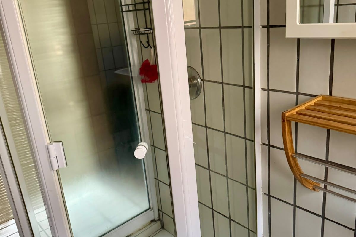 A functional bathroom featuring a corner shower enclosure with white tiled walls and flooring, complemented by a wall-mounted storage rack.