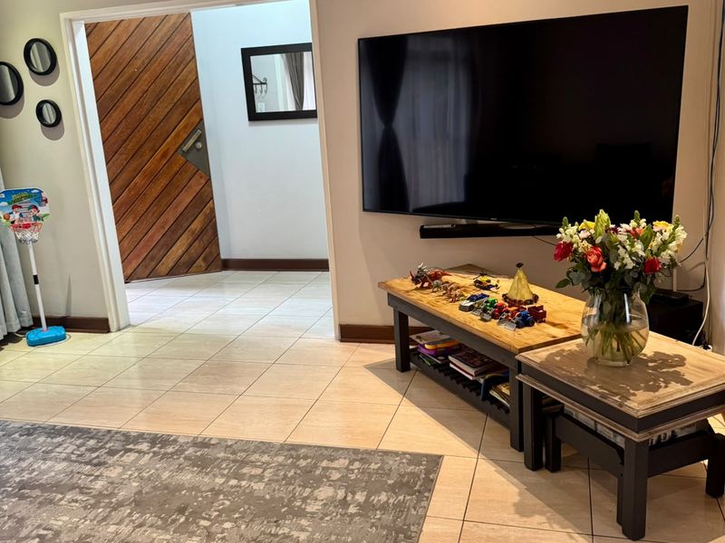 A living room area featuring tiled flooring and a wall-mounted television, with a doorway leading to an adjacent space.