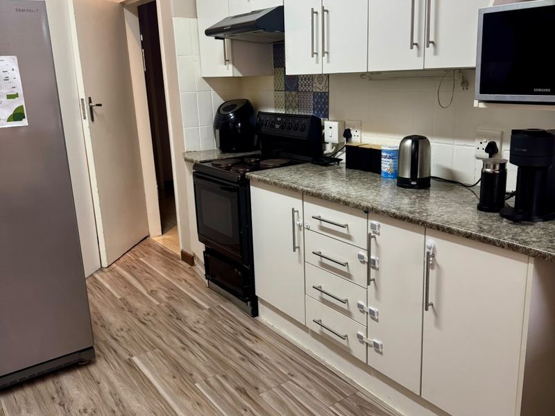 A functional kitchen featuring white cabinetry, granite-look countertops, a built-in extractor fan, and wood-look laminate flooring.