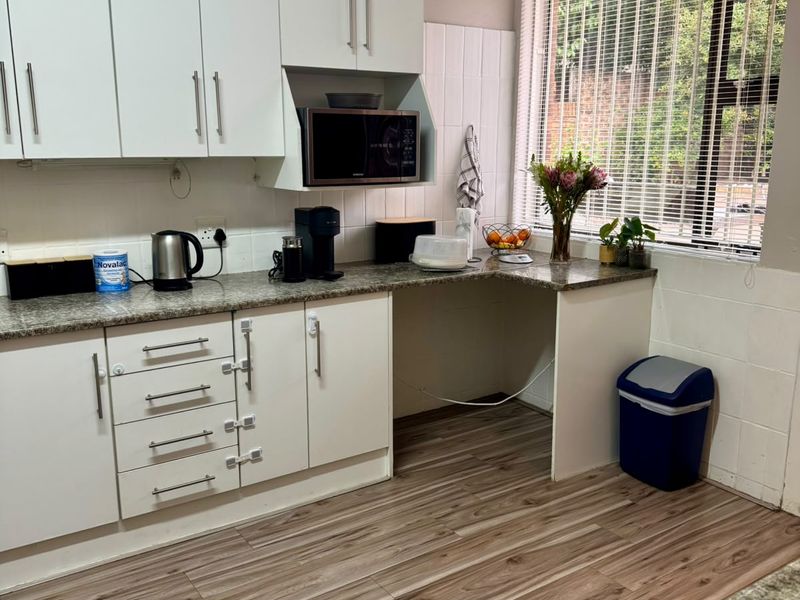 A functional kitchen featuring white cabinetry, granite-look countertops, wood-look laminate flooring, and a built-in microwave space with natural light from a window.