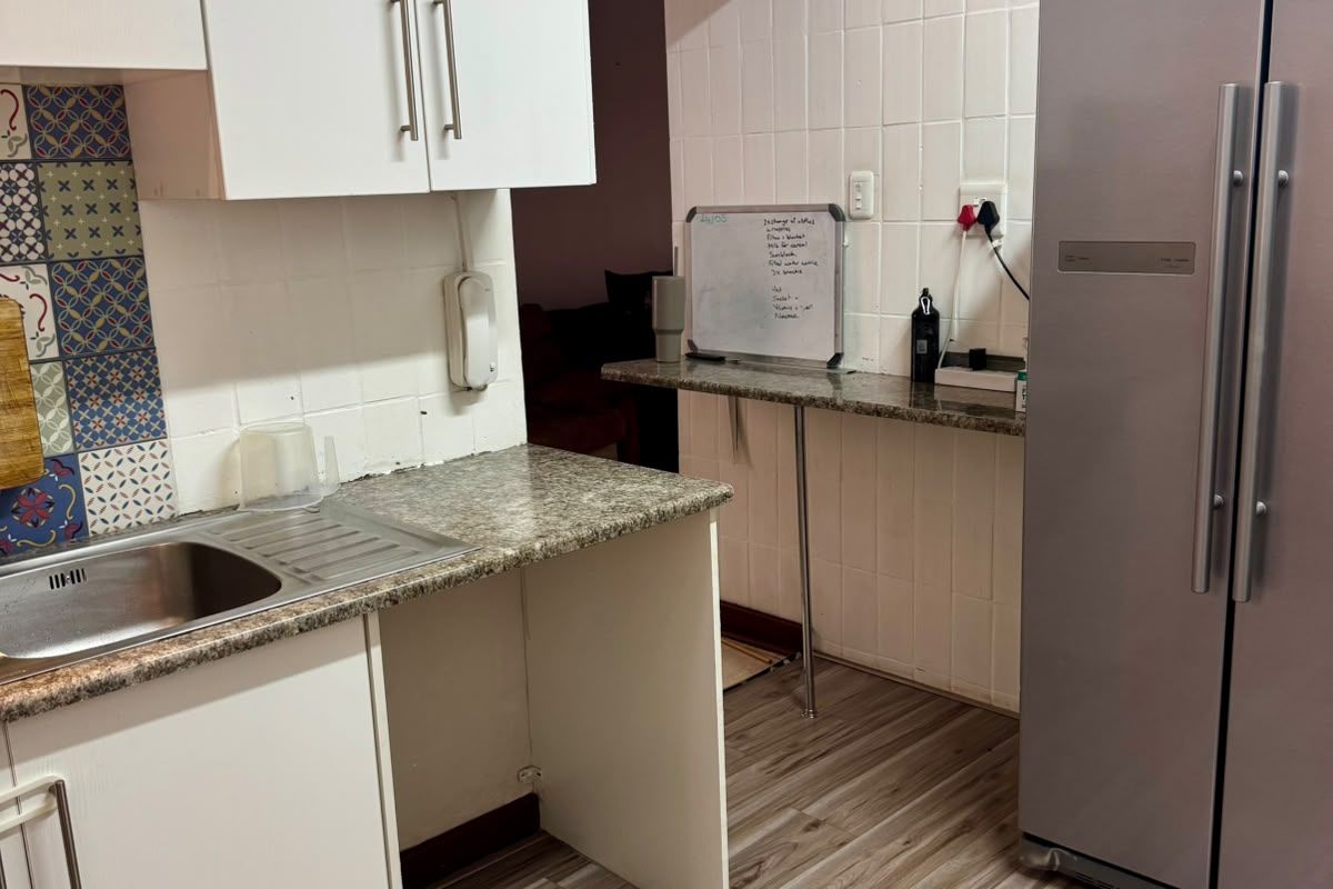 A functional kitchen area featuring white cabinetry, granite countertops, a stainless steel sink, and tiled splashbacks with decorative accents.