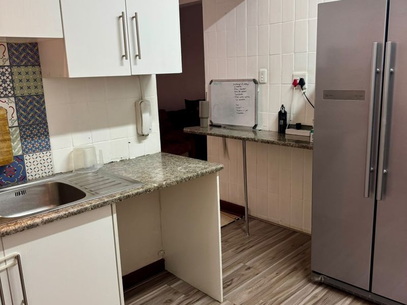 A functional kitchen area featuring white cabinetry, granite countertops, a stainless steel sink, and tiled splashbacks with decorative accents.