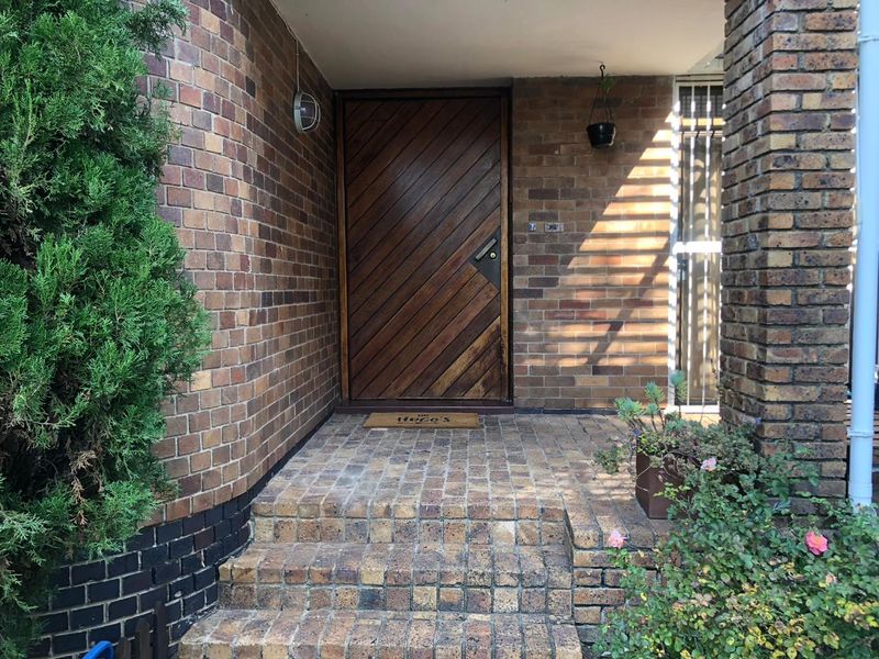 A covered entrance featuring a solid timber diagonal-plank door, brick steps, and exposed face-brick walls.