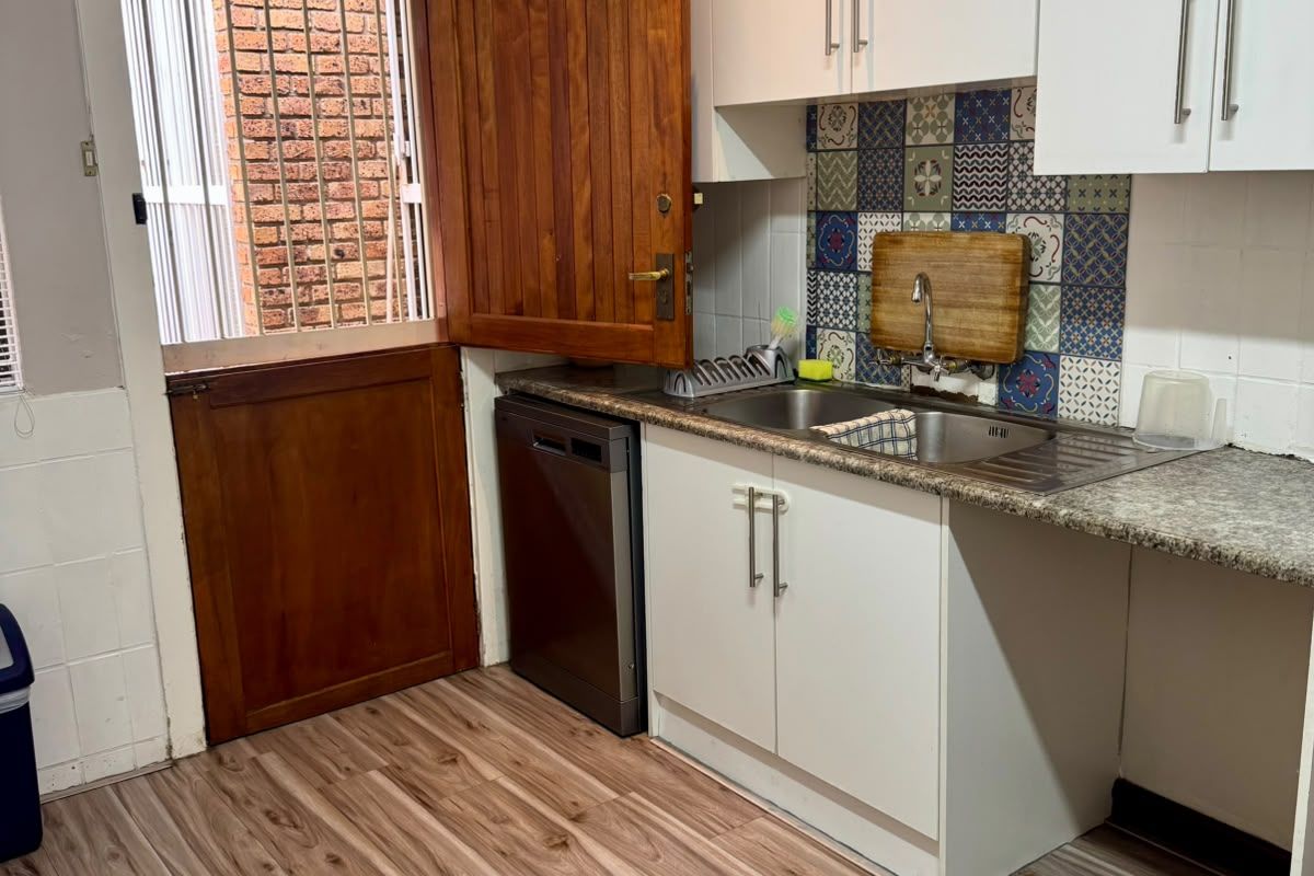 Functional kitchen area featuring white cabinetry, patterned tile splashback, stainless steel sink, and direct access to an exterior door.