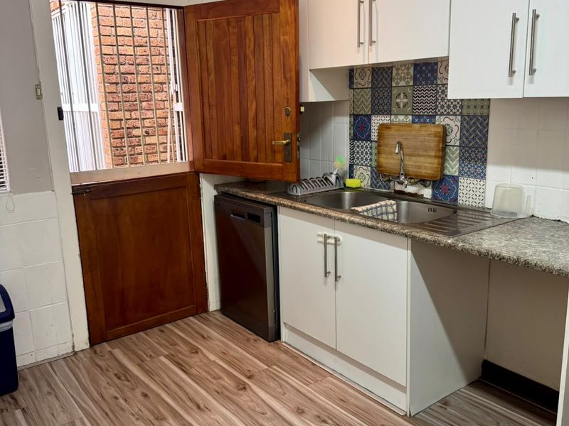 Functional kitchen area featuring white cabinetry, patterned tile splashback, stainless steel sink, and direct access to an exterior door.