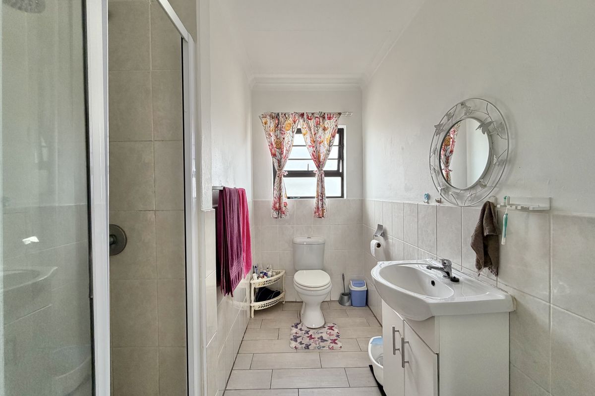 A functional bathroom featuring a glass-enclosed shower, a vanity basin with storage, and a toilet, finished with neutral wall and floor tiling.