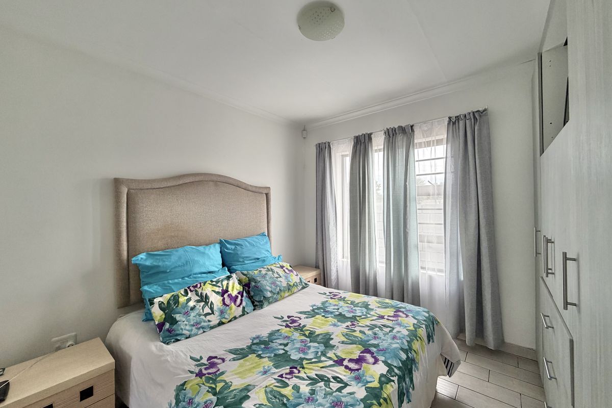 A bright bedroom featuring built-in wardrobes, tiled flooring, and large windows with security bars, offering a clean and functional living space.