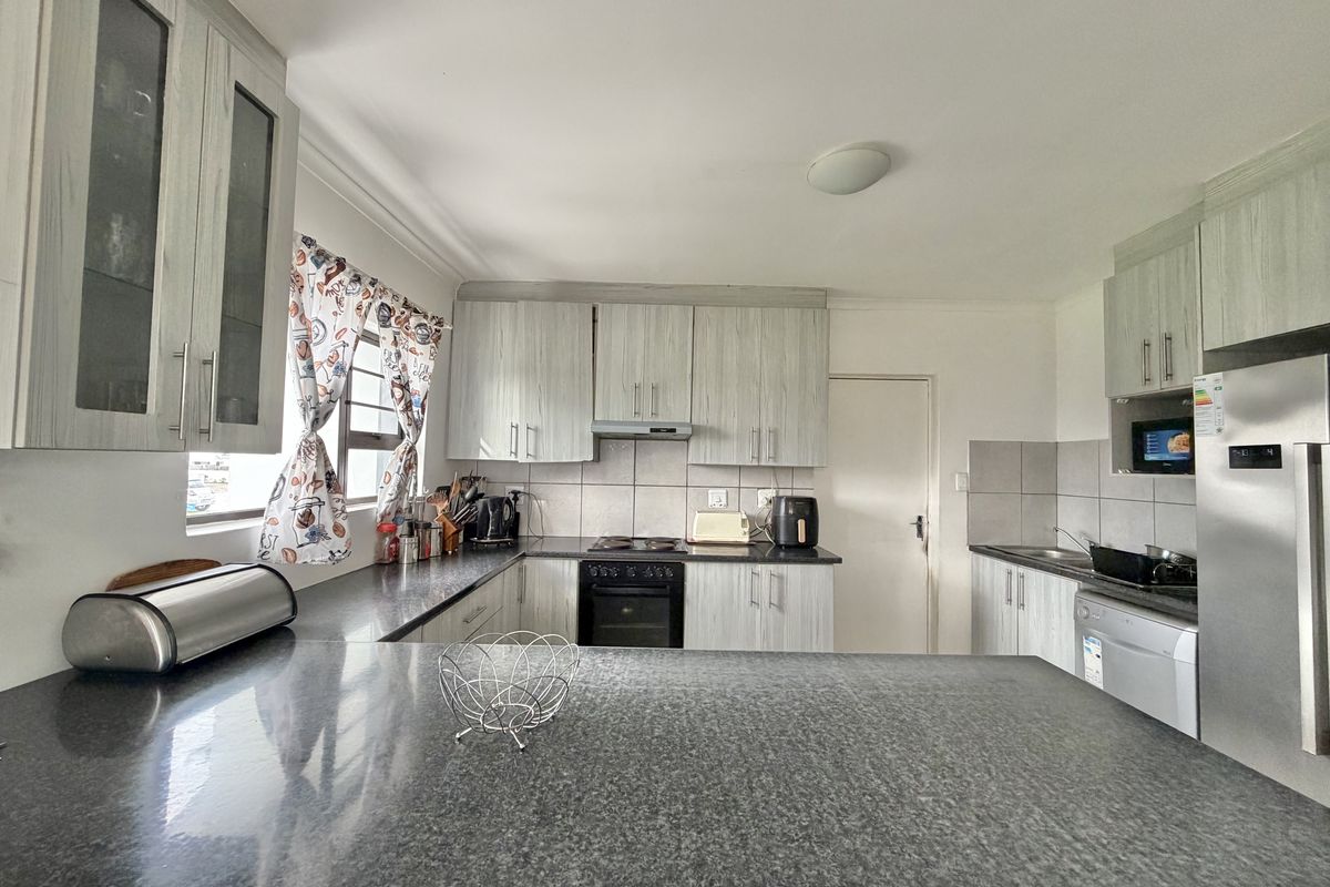 Functional kitchen featuring light wood-grain cabinetry, dark granite countertops, built-in oven, hob, and extractor fan with a convenient breakfast bar layout.