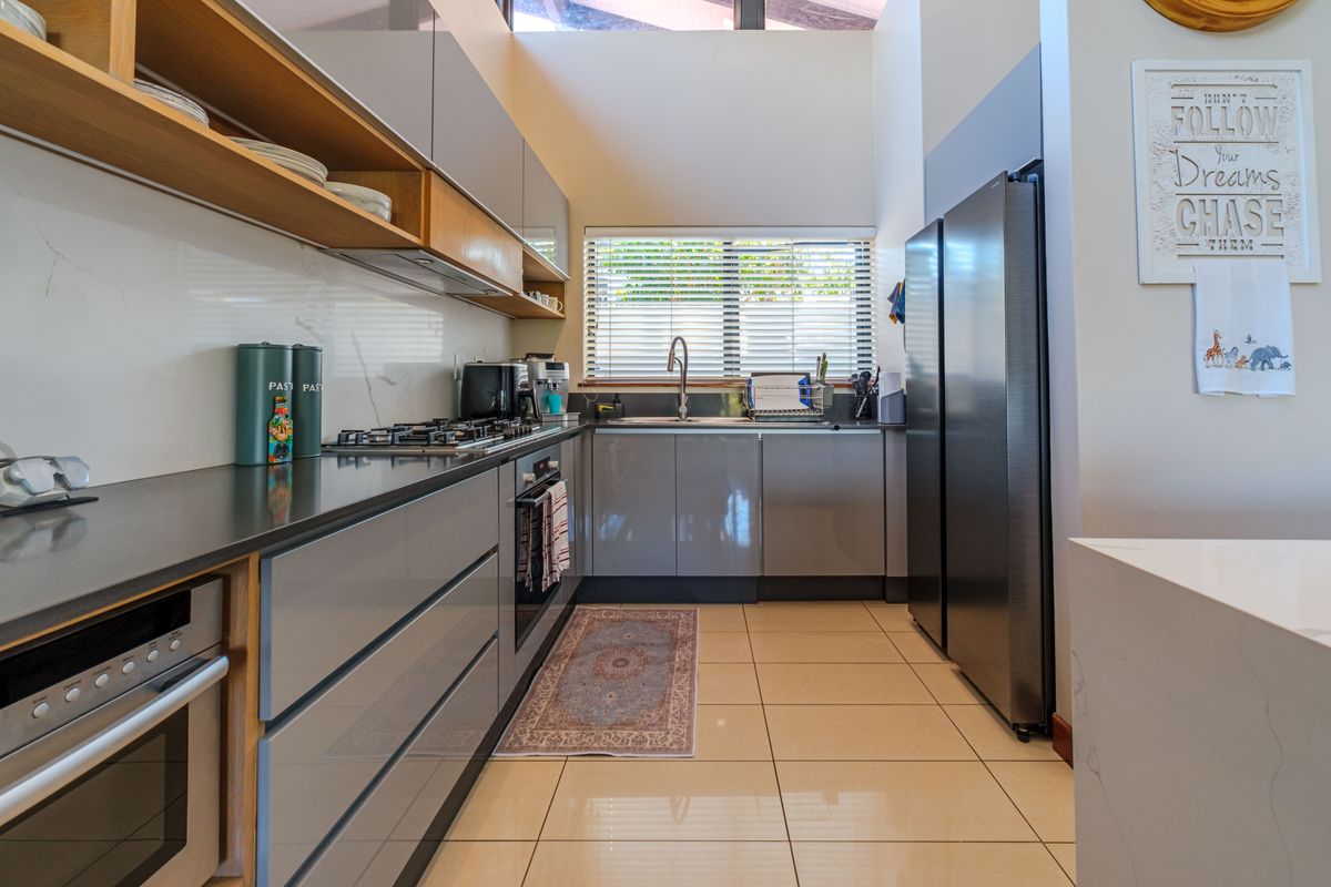 Modern kitchen featuring sleek grey cabinetry, stone countertops, integrated oven, gas hob, and high ceilings with ample natural light.