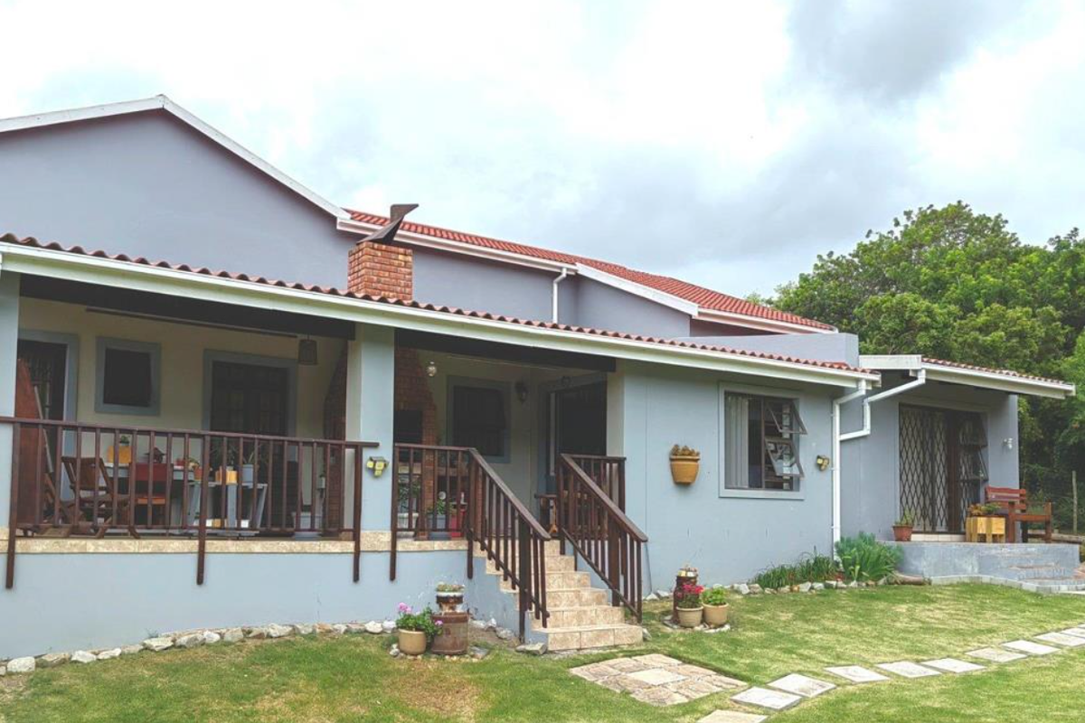 Rear view of the house featuring a covered patio with a built-in brick fireplace, tiled stairs, and a landscaped garden area.