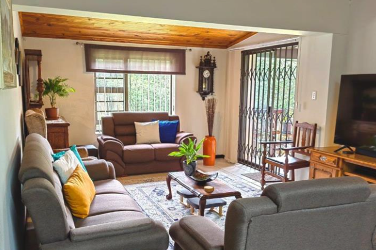 A comfortable living room featuring a vaulted timber-clad ceiling, tiled flooring, and sliding glass doors with security gates leading to the exterior.