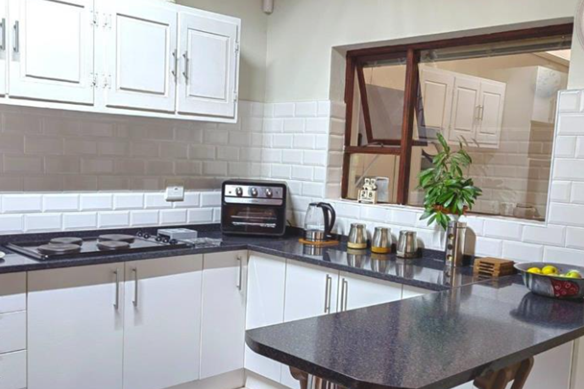 A functional kitchen featuring white cabinetry, dark granite countertops, a built-in hob, and classic white subway tile splashbacks with a breakfast bar area.