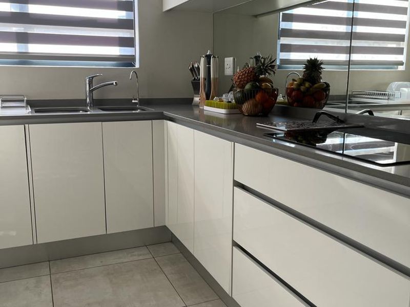 Modern kitchen featuring sleek white cabinetry, stone countertops, a mirrored backsplash, integrated hob, and large format floor tiles.