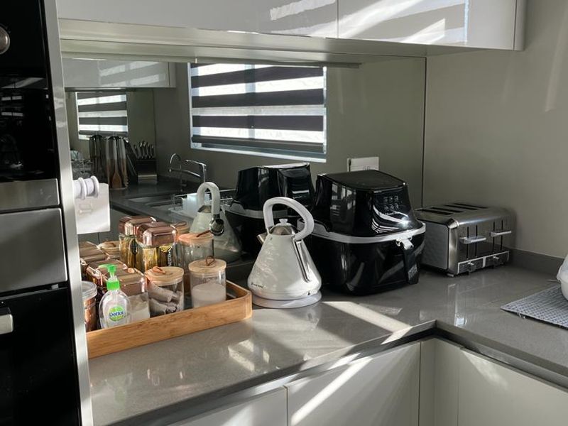 Modern kitchen featuring sleek white cabinetry, stone countertops, and a mirrored splashback, creating a bright and contemporary culinary space.